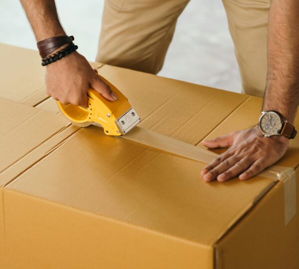 Unrecognizable man sealing box with duck tape while preparing for moving out
